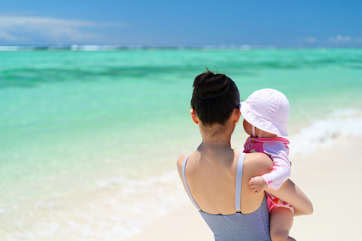 完全防備の赤ちゃんを抱っこして宮古島の海を見つめる若いお母さん